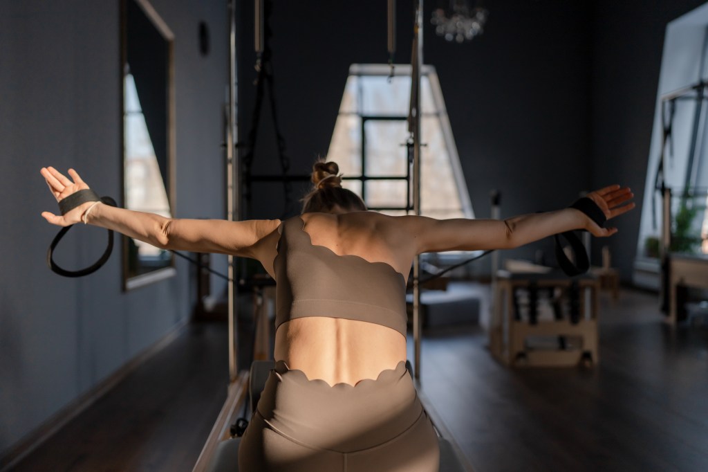 Person performing a Pilates exercise using resistance equipment in a fitness studio.