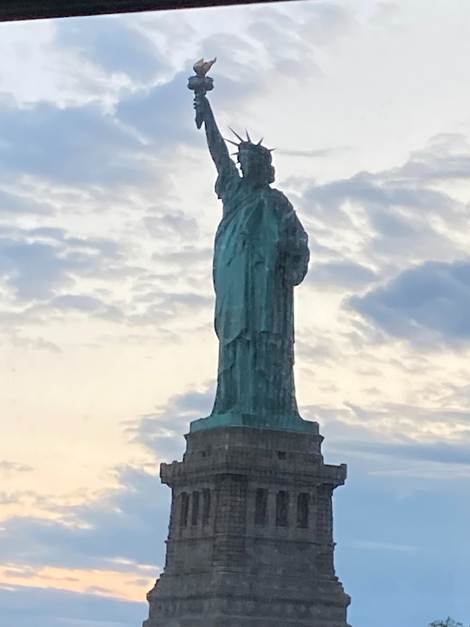 Statue of Liberty against a cloudy sky during sunset, holding a torch.